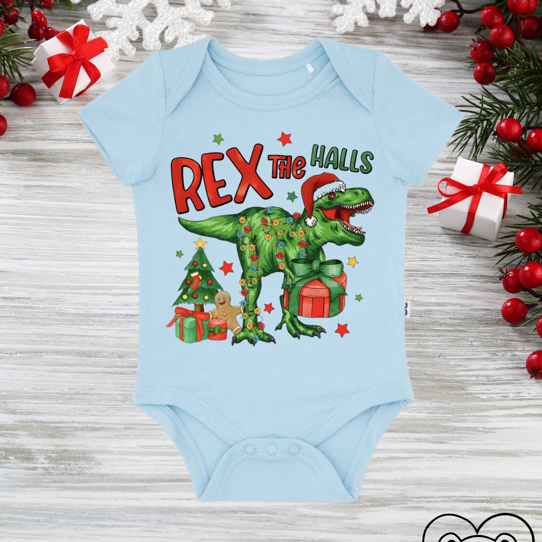 Light blue baby onesie with a Christmas-themed dinosaur design on a wooden surface with holiday decorations.